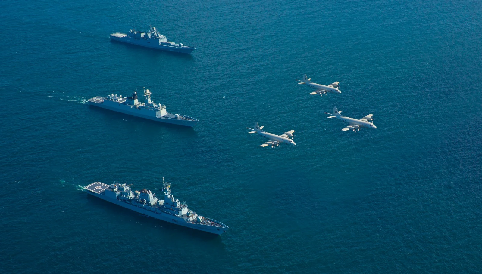 Pakistan Navy surface ships at sea with aircraft flying overhead.
