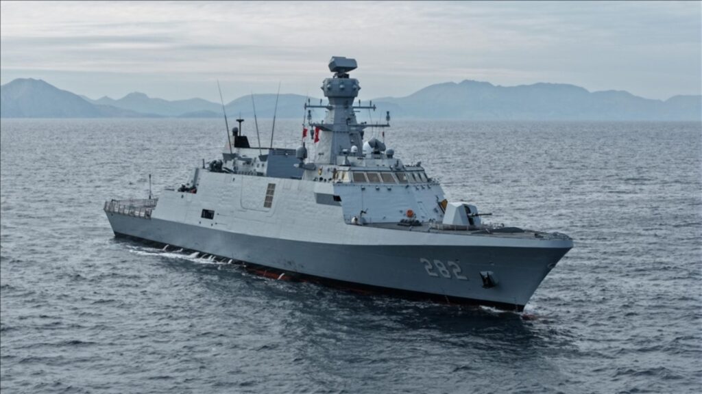 Gray military destroyer with hull number 282 cruising the calm sea with distant mountains on the horizon.