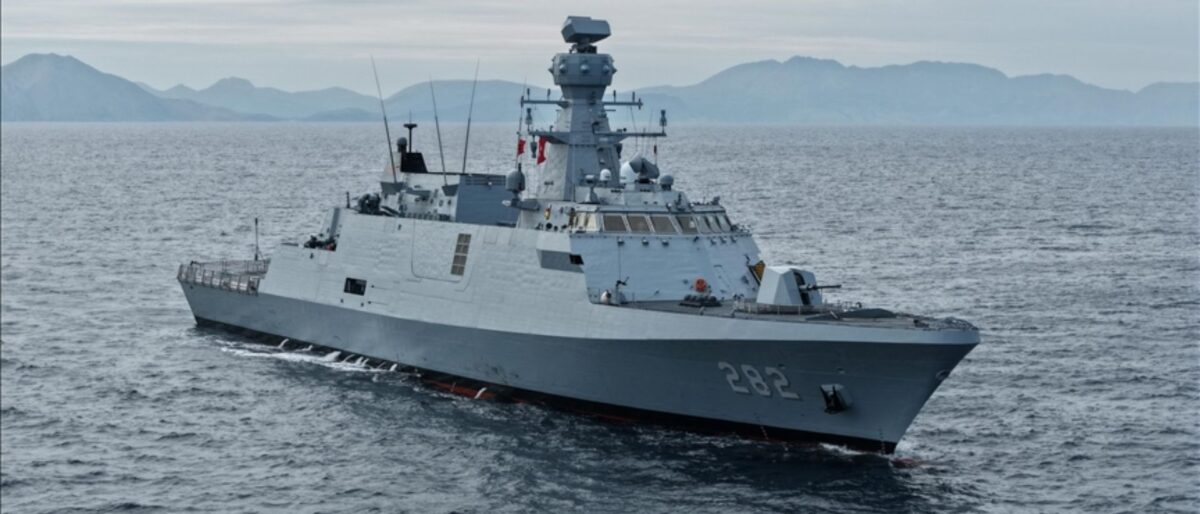 Gray military destroyer with hull number 282 cruising the calm sea with distant mountains on the horizon.