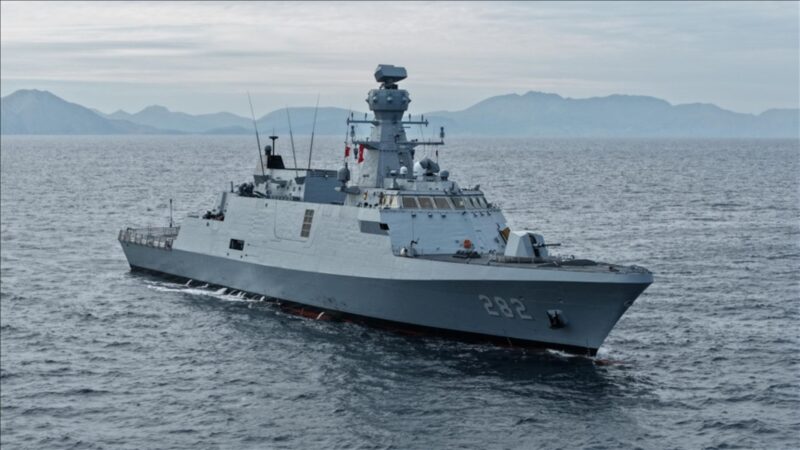 Gray military destroyer with hull number 282 cruising the calm sea with distant mountains on the horizon.