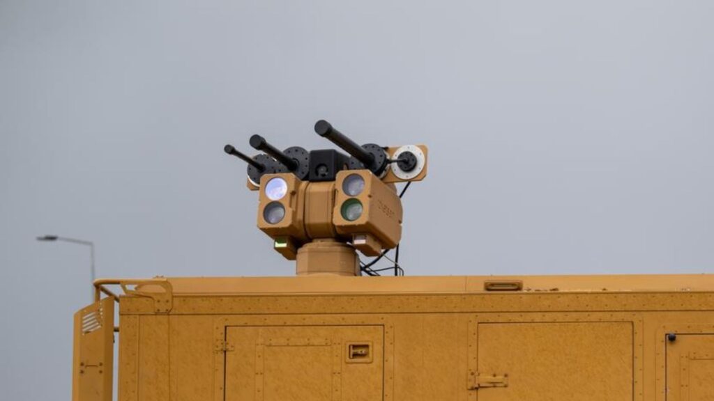Yellow utility vehicle with a multi-lens traffic signal array on top, against a gray sky.