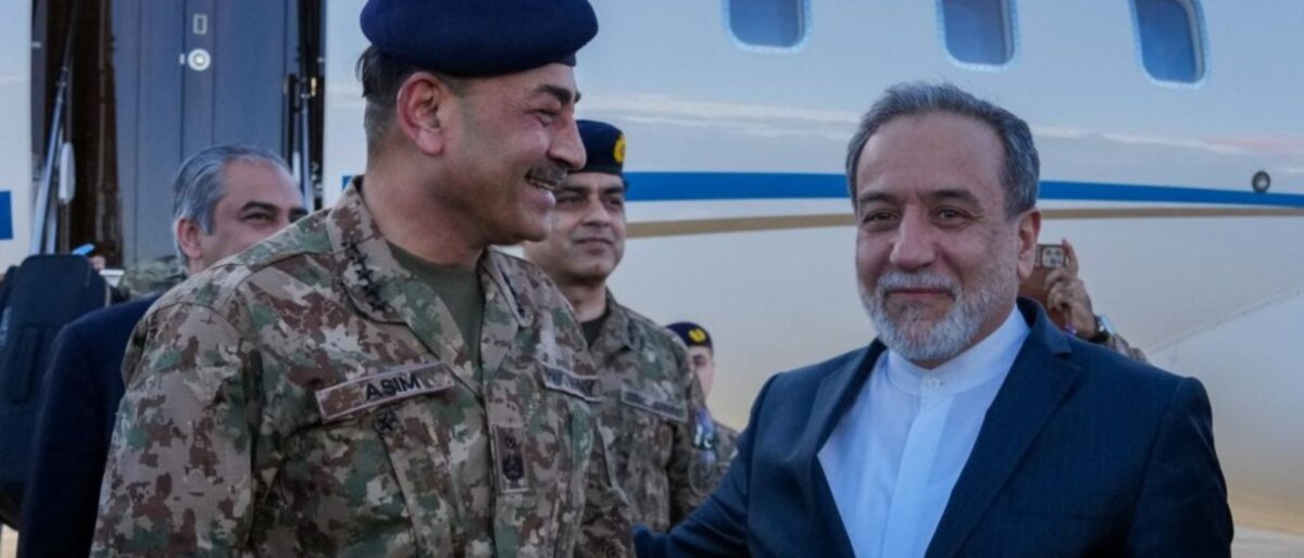 Military officer in camouflage with a blue beret smiling beside a civilian man near a plane.