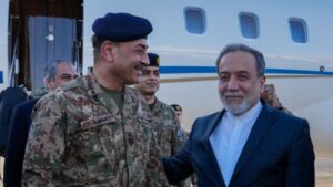 Military officer in camouflage with a blue beret smiling beside a civilian man near a plane.