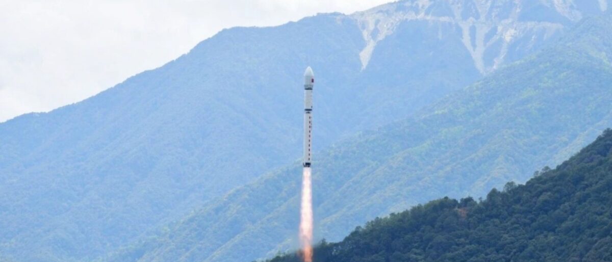 Rocket launch rising from a mountainside with a fiery exhaust plume trailing behind the rocket toward a cloudy sky
