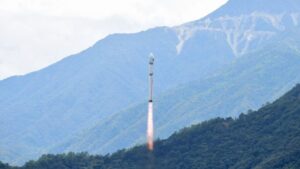 Rocket launch rising from a mountainside with a fiery exhaust plume trailing behind the rocket toward a cloudy sky