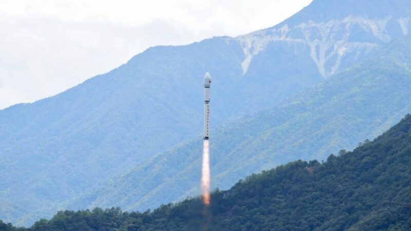 Rocket launch rising from a mountainside with a fiery exhaust plume trailing behind the rocket toward a cloudy sky