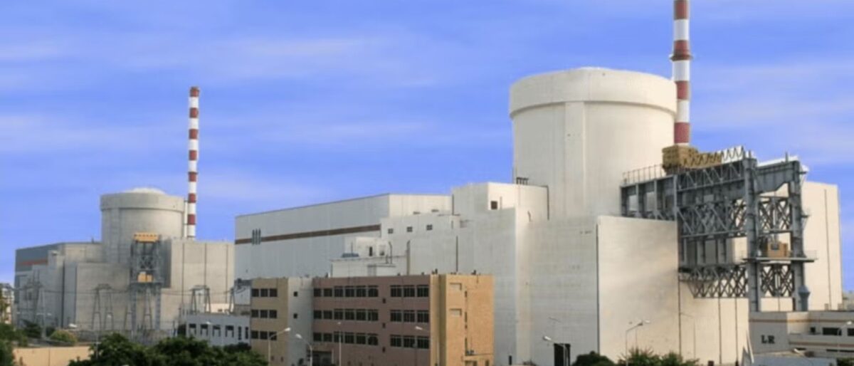 Industrial power plant with cooling towers and striped chimneys under a blue sky.