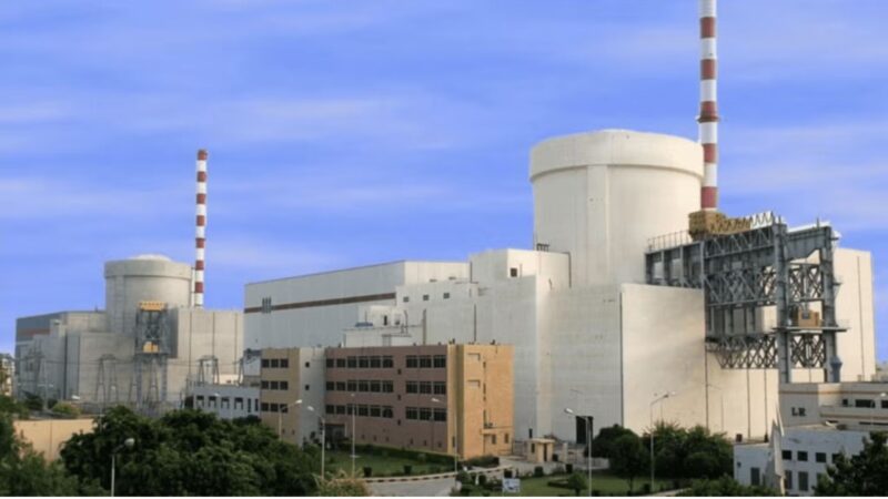 Industrial power plant with cooling towers and striped chimneys under a blue sky.