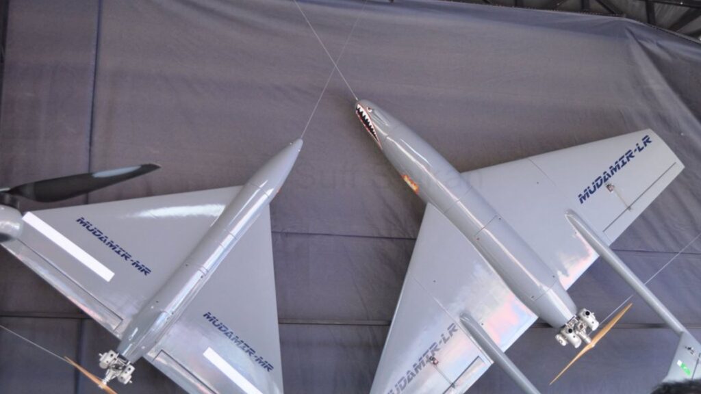 Silver aircraft model on display, suspended by wires, showing wings and fuselage with blue markings along the side.