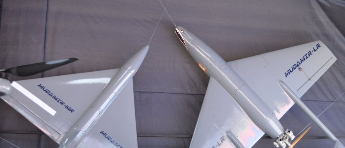 Silver aircraft model on display, suspended by wires, showing wings and fuselage with blue markings along the side.