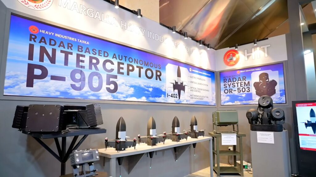 Exhibition booth displaying a large banner for radar-based autonomous interceptor P-905 with models and equipment on display.