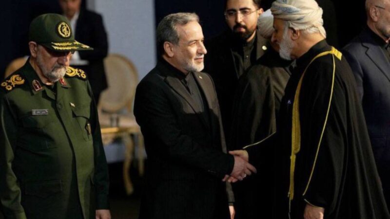 Three men in formal attire greet each other: a high-ranking military officer in a green uniform on the left, a man in a black suit in the center, and a cleric with a white turban on the right.