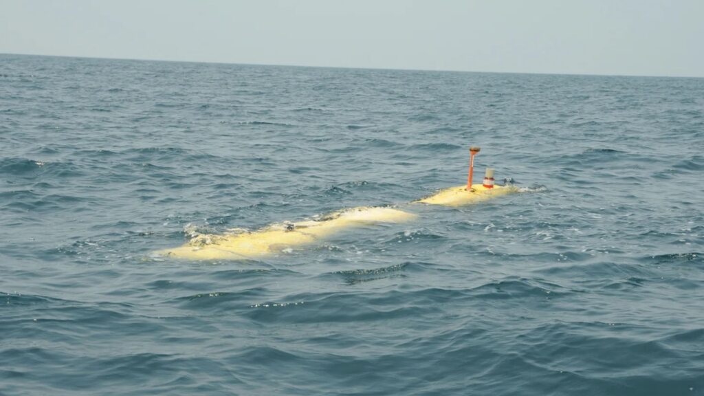 Yellow submarine-like submersible drifting on the surface of the blue ocean, with an orange periscope/antenna and top equipment visible.