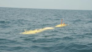 Yellow submarine-like submersible drifting on the surface of the blue ocean, with an orange periscope/antenna and top equipment visible.