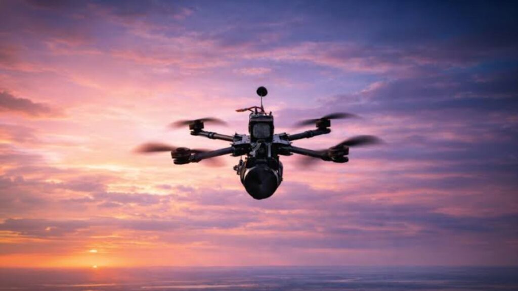 Hexacopter drone with camera hovering over a sunset-lit ocean on the horizon.