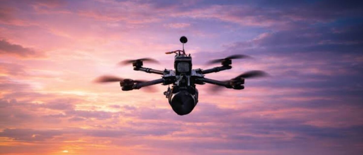 Hexacopter drone with camera hovering over a sunset-lit ocean on the horizon.