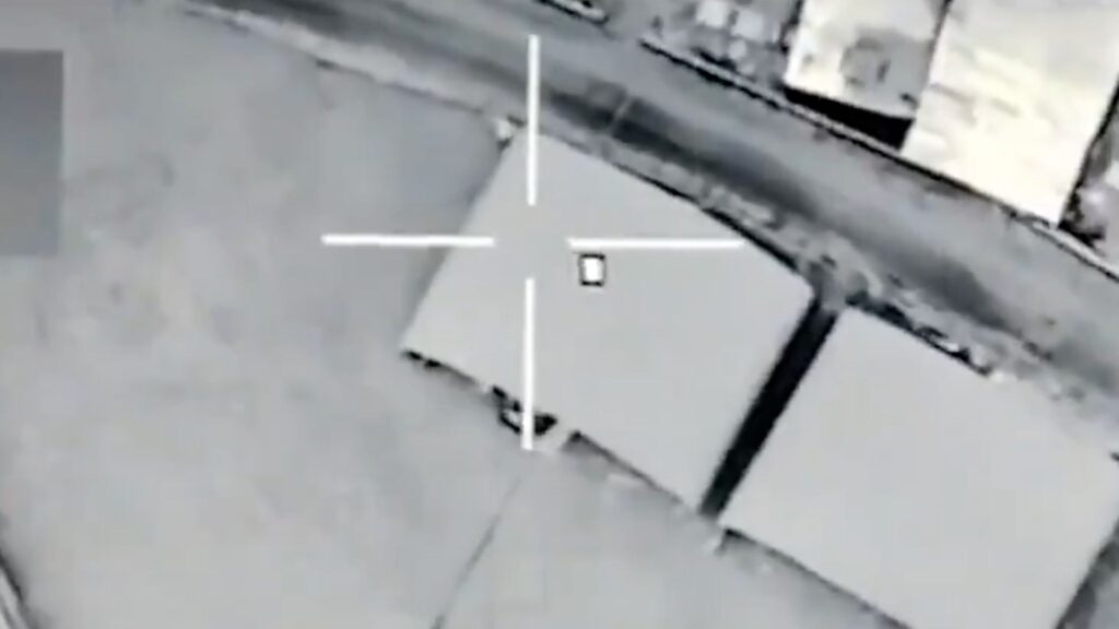 Drone-style targeting view: a gray rooftop with a white crosshair centered on a gray crate.