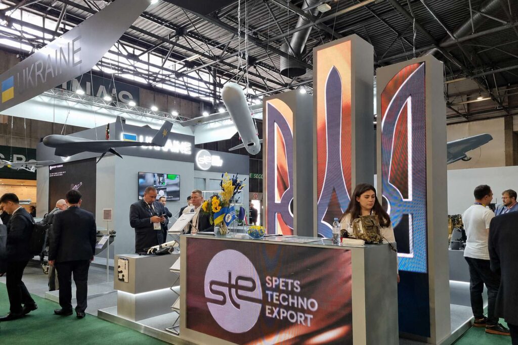 Ukraine's national pavilion at Eurosatory 2026 with SpetsTechnoExport branding and Ukrainian UAVs suspended above the stand