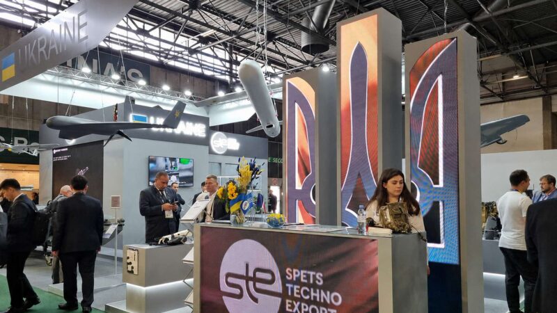 Ukraine's national pavilion at Eurosatory 2026 with SpetsTechnoExport branding and Ukrainian UAVs suspended above the stand