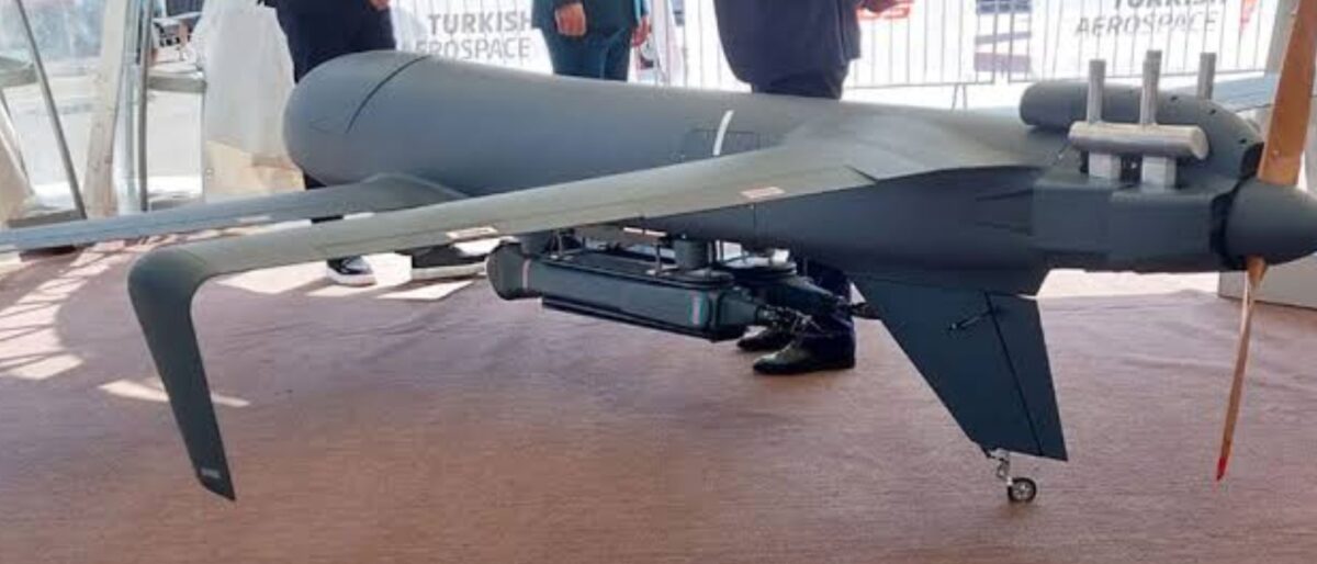 Large unmanned drone on display at an aerospace expo, with attendees and Turkish Aerospace branding in the background, indoors.