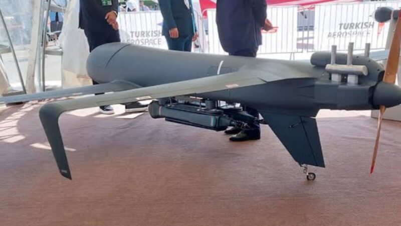 Large unmanned drone on display at an aerospace expo, with attendees and Turkish Aerospace branding in the background, indoors.