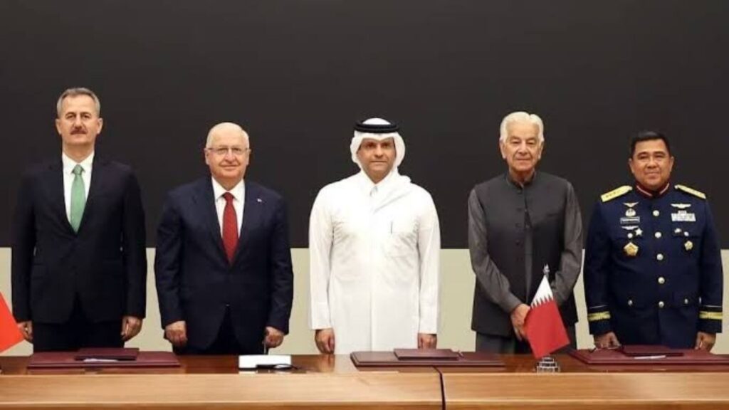 Five men in formal attire stand behind a conference table with documents, posing for a formal signing ceremony after a meeting.