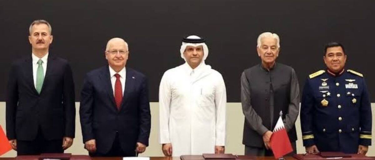 Five men in formal attire stand behind a conference table with documents, posing for a formal signing ceremony after a meeting.