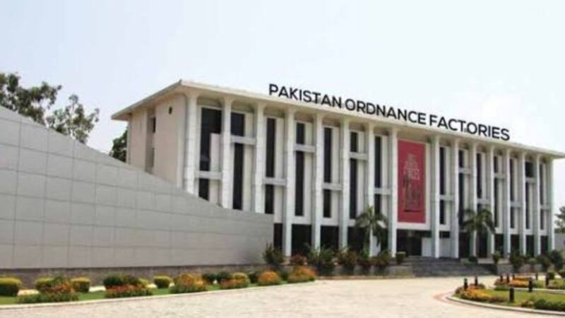 Front view of the Pakistan Ordnance Factories building with tall columns and landscaped grounds below the sign.”