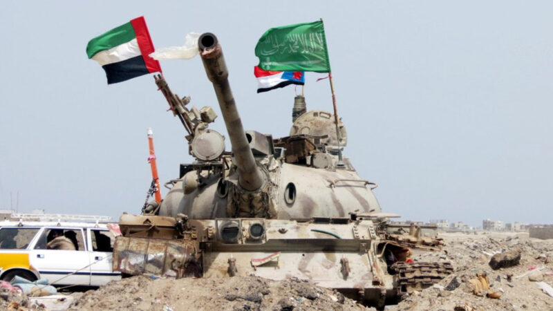 Armored tank in a dusty desert with UAE and Saudi flags mounted on its turret.