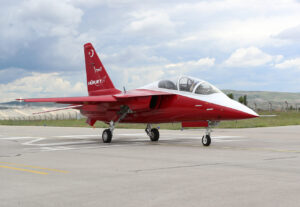 Red and white HÜRJET jet trainer with its landing gear down on an apron
